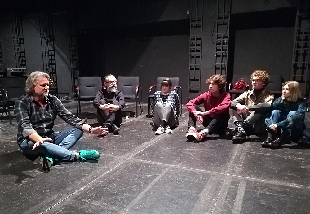 Scena Miniatura. Na podłodze siedzi grupa młodzieży. Obok nich dramaturg oraz dyrektor teatru. Rozmawiają.