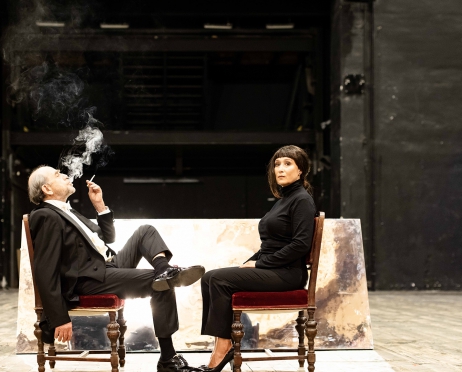 Naprzeciwko siebie, na bordowych stylizowanych krzesłach siedzą aktorzy Jan Peszek i Dominika Bednarczyk. Obydwoje ubrani są na czarno, siedzą w pomieszczeniu pomalowanym na czarno. Aktor ma założoną nogę na nogę, luźno puszczoną rękę, w drugiej ręce trzyma papierosa. W górę wydmuchuje dym z ust. Kobieta siedzi naprzeciwko, ale odwraca głowę w stronę aparatu. Jest poważna.