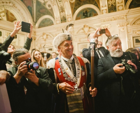 Na zdjęciu grupa osób. Między innymi fotografowie. Robią zdjęcia. Śmieją się. W centralnej części mężczyzna z bractwa kurkowego. Ubrany w strój bractwa. Zdjęcie zrobione we foyer Teatru.