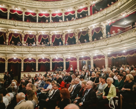 Na zdjęciu rozświetlona widownia Dużej Sceny. W tle loże na balkonach. Osoby na parterze patrzą w stronę sceny. Słuchają z zaciekawieniem tego co się tam dzieje.