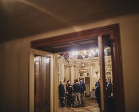 Na pierwszym planie otwarte szklane drzwi widoczne do połowy. W tle grupy ludzi rozmawiających ze sobą we wnętrzach Teatru Słowackiego, we foyer.