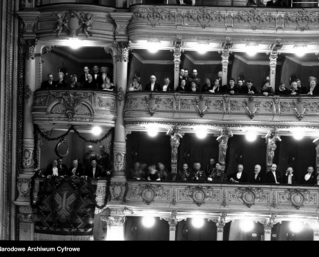 Na zdjęciu loże pierwszego i drugiego piętra widowni Dużej Sceny Teatru im. Juliusza Słowackiego w Krakowie. Jedna z lóż ozdobiona jest girlandami kwiatowymi. Widzowie ubrani są w odświętne, eleganckie ubrania. Zdjęcie czarno-białe