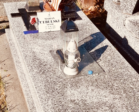 Zdjęcie grobu Mariana Cebulskiego na cmentarzu. Nagrobek jest kamienny, płaski. Na płycie nagrobka stoją znicze.