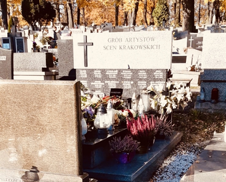 Zdjęcie grobu Artystów Scen Krakowskich na cmentarzu. Na płycie wiele kwiatów i zniczy, wokół inne groby.
