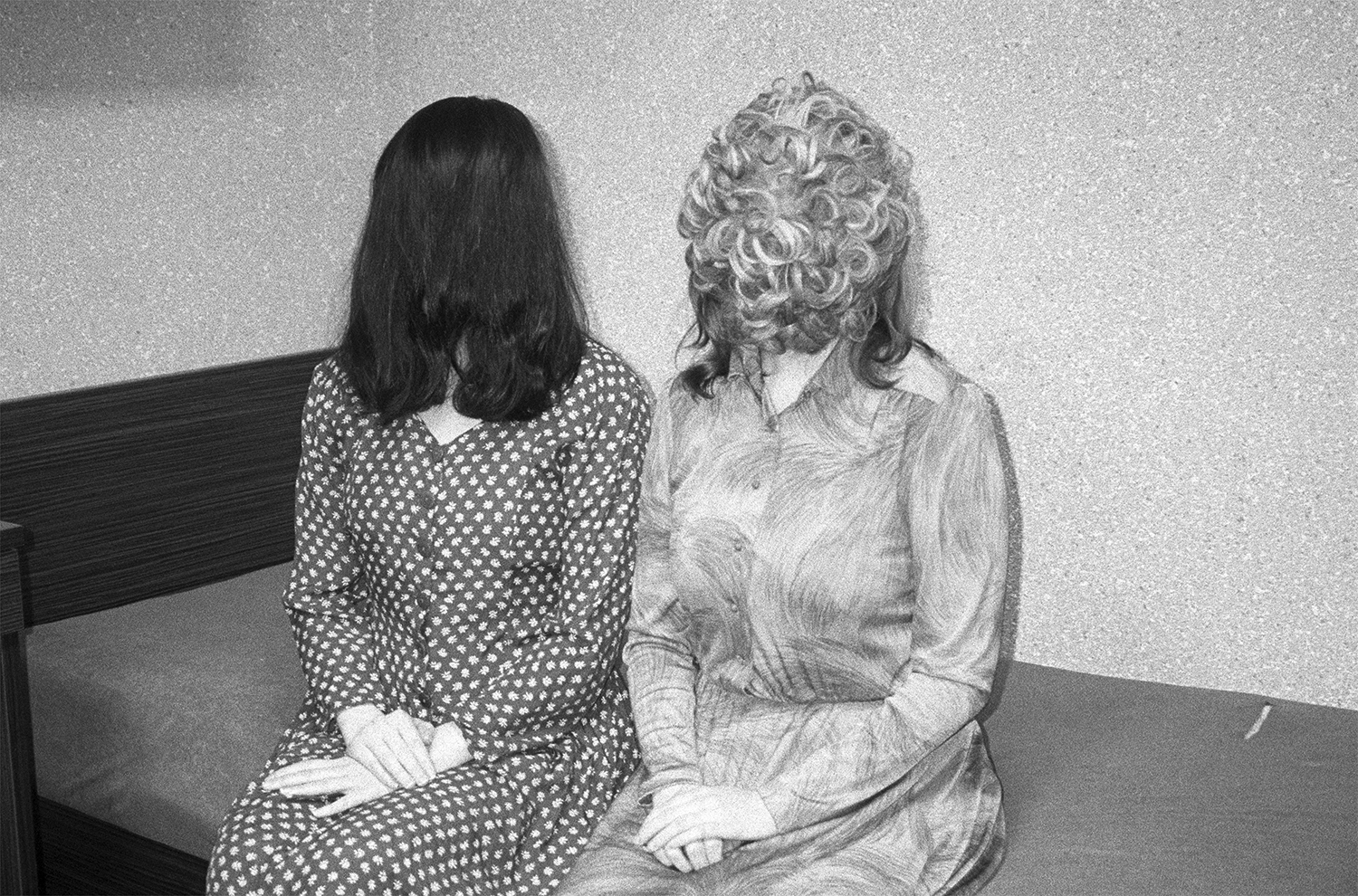 Czarno-białe zdjęcie przedstawiające dwie kobiety siedzące na wersalce. Ich włosy zasłaniają całą twarz. Dłonie mają złożone na kolanach. Pierwsza kobieta ma na sobie sukienkę w białe grochy. Druga koszulową sukienkę we wzory. Tło jest białe.