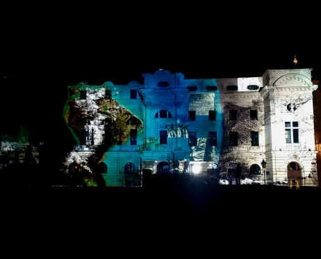 Zdjęcie bocznej ściany Teatru Słowackiego nocą. Na budynku wyświetlona jest projekcja biało-niebiesko-zielona. Wokół panuje ciemność.