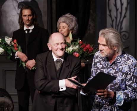 Na zdjęciu dyrektor Teatru Krzysztof Głuchowski ubrany w błękitną koszulę w kwiaty wykonuje gest jakby miał przytulić starszego mężczyznę ubranego w smoking. Ten wykonuje ten sam gest. W tle młody mężczyzna i dwie kobiety. Klaszczą i uśmiechają się.