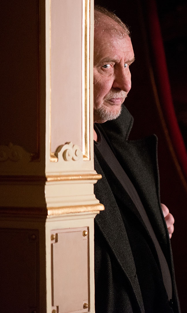 Aktor Andrzej Grabowski stoi za filarem we wnętrzach Teatru Słowackiego. Widoczna twarz i fragment marynarki. Spogląda w stronę obiektywu. Wygląda tajemniczo, jakby podglądał