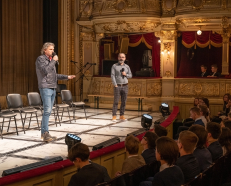 Na zdjęciu scena oraz fragment widowni. Na scenie dyrektor Teatru, w ręku trzyma mikrofon. Coś mówi. Za nim pięć pustych czarnych krzeseł. Obok krzeseł stoi mężczyzna około czterdziestu sześciu lat. W dłoni trzyma mikrofon. JEdną dłoń trzyma w kieszeni. Patrzy w kierunku dyrektora Teatru. W prawym rogu fragment loży parterowej w niej siedzą młodzi ludzie. Tłem jest opuszczona zielona kotara za sceną.