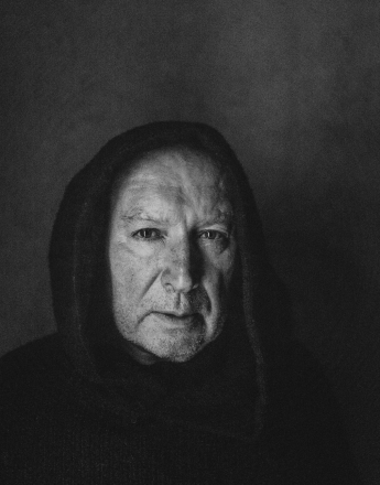 Czarno-biały portret Sławomira Rokity w habicie zakonnika. Stary aktor patrzy enigmatycznie z półprofilu w obiektyw. Na głowie ma kaptur. Ujęcie obejmuje wyłącznie twarz i ramiona.