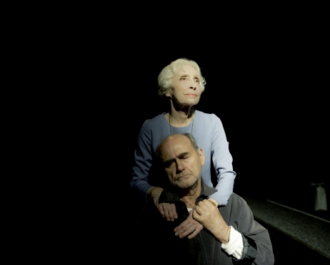 Na zdjęciu Anna Polony i Jan Peszek. Aktorka stoi za plecami siedzącego mężczyzny, opiera dłonie na jego torsie. Patrzy z nostalgią przed siebie. Mężczyzna ma zamknięte oczy i dłońmi obejmuje ręce kobiety.