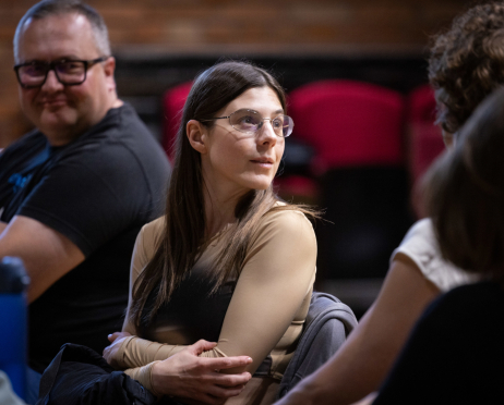 W sali prób Teatru przy ulicy Radziwiłłowskiej przy stole siedzą inspicjent Bartłomiej Oskarbski i 33-letnia aktorka Magdalena Osińska podczas próby czytanej spektaklu „Układ Scalony”.  Bartłomiej Oskarbski, mężczyzna o krótko przystrzyżonych siwiejących włosach ma na sobie czarny T-shirt i ciemne okulary w grubych oprawkach. Uśmiecha się, spoglądając w stronę pozostałych uczestników. Obok siedzi Magdalena Osińska,  kobieta z długimi, prostymi ciemnobrązowymi włosami i jasną cerą. Ma na nosie delikatne okulary w cienkich oprawkach oraz beżową bluzkę z długimi rękawami. Siedzi z rękami skrzyżowanymi, odwrócona w prawo i uważnie słucha osoby znajdującej się poza kadrem. W tle widoczne są czerwone teatralne krzesła.