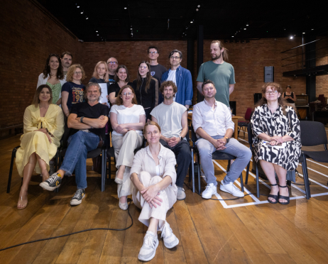 Grupowy portret wykonany w sali prób Teatru przy ulicy Radziwiłłowskiej. Na zdjęciu znajduje się obsada spektaklu „Układ Scalony”, a także scenarzysta, reżyser, producent, inspicjent, dyrektor teatru oraz pozostali członkowie zespołu realizatorskiego. Uczestnicy ustawieni są w trzech rzędach, część siedzi na krzesłach, część stoi za nimi, a jedna osoba siedzi na podłodze na pierwszym planie. Większość uśmiecha się w stronę obiektywu. Ubrani są swobodnie, w jasne koszule, T-shirty, sukienki i dżinsy. W tle widoczne są ceglane ściany, drewniana podłoga oraz przestrzeń sali prób z krzesłami i stołami.